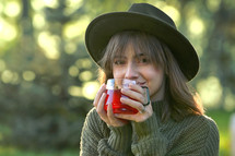 Young Woman in a hat Holding a Hot Tea Cup outdoors in fall 
