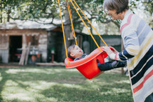 a grandmother pushing a toddler girl on a swing 