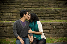 man and woman sitting outdoors kissing