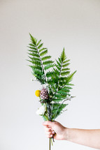 hand holding out a bouquet of flowers and ferns 