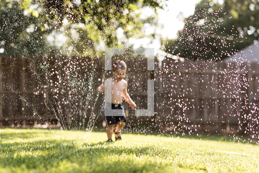 a boy playing in a sprinkler 