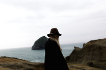 woman in a hat standing between rocks on a beach 