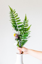 placing ferns and flowers in a vase 