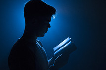 a man reading a Bible illuminated in darkness 