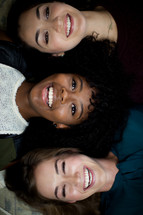 Three smiling young women lying with their heads close together.