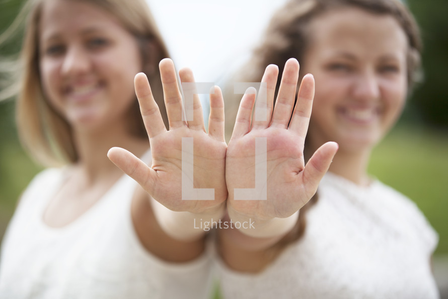 Two girls pushing their hands out toward the camera. 