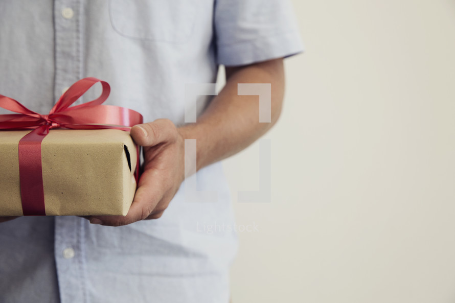 A man holding a gift wrapped in brown paper and a red bow.
