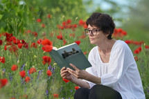 a woman reading a book sitting in a field of wildflowers 