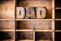 Wooden letters spelling "Dad" on a wooden bookshelf.