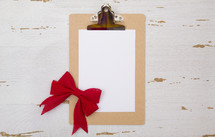 clipboard with white paper and red bow 