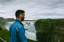 a man standing looking out at a waterfall 