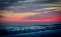 Ocean waves rolling into shore under a red hazy sky.