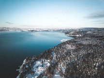 aerial view over a snow covered evergreen forest and lake 