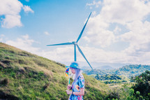 a woman holding pinwheels beside a wind turbine 