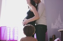 an expecting couple hugging as their toddler son watches 