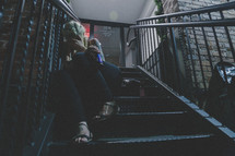 a girl holding a beer bottle sitting on steps outdoors at night 