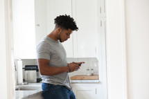 man texting on his cellphone in a kitchen 