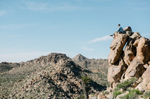 a man sitting on a rock looking out at a desert 
