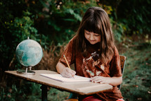 school girl writing at her desk with a globe