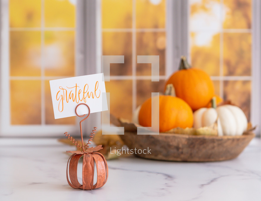 Orange and white pumpkins with a grateful sign in front of autumn window