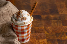 A Pumpkin Spice Latte Topped with Whipped Cream in a Disposable Cup on a Wood Background