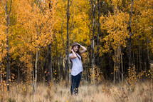 a teen girl in a hat standing in a fall forest 