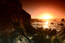 sunset over the ocean along a rocky shore 