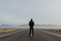 man in a hoodie standing in the center of a highway 