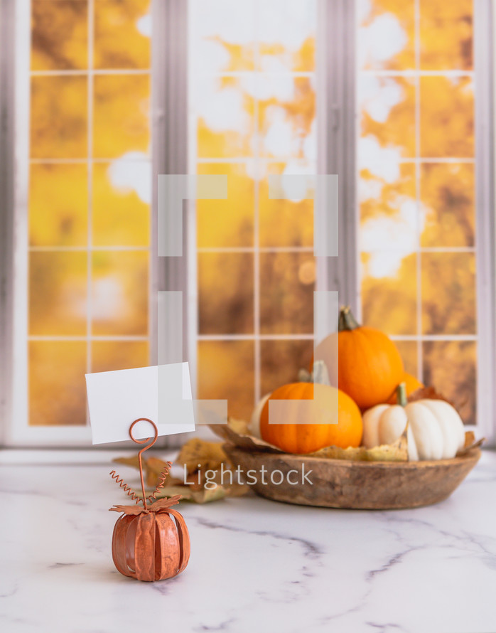 Orange and white pumpkins with a blank sign in front of autumn window