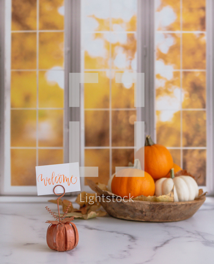 Orange and white pumpkins with a welcome sign in front of autumn window