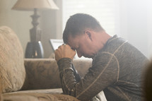 A mature middle aged man praying and leaning on sofa