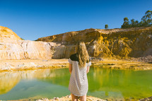 A girl standing near a pool of water in a quarry.