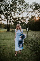 teen girl carrying a blanket walking in the grass