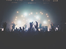 silhouettes of raised hands of audience members at a concert 