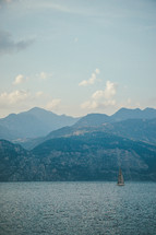 sailboat in water in front of a mountainous island 