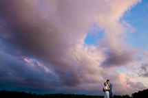 A bride and groom standing together under a cloudy sky.