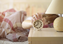 woman in bed turing off her alarm clock 