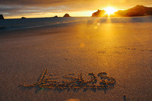 Jesus written in the sands of a beach at sunset 