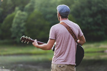 A young man playing a guitar outside.