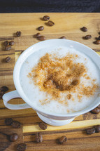 Delicious home made Cappuccino, in a white cup, on a wooden table. With coffee beans. Home made Coffee.