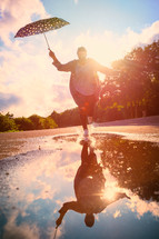 woman having fun after rain, running in pond with her umbrella at sunset