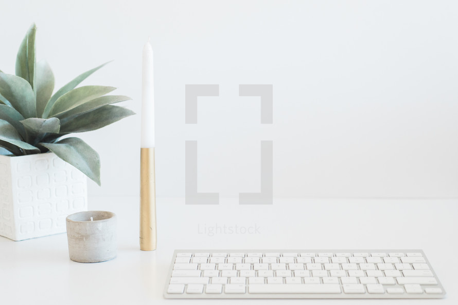 A white keyboard, succulent plant and candle on a white surface.