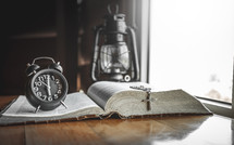 alarm clock, oil lamp, cross, and open Bible 