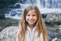 smiling child standing in front of a waterfall 