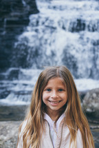 smiling girl standing in front of a waterfall 