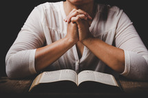 Woman with folded hands praying with open Bible