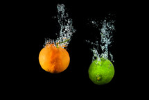 Fresh lime and orange in water with air bubbles water splash isolated on black