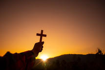 arm holding up a cross against an orange sky 