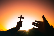 arms holding up a cross against an orange sky 