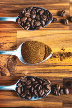 Spoons with coffee powder and coffee beans, laying down on a wooden background.